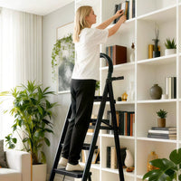 Femme debout sur l'escabeau 4 marches noir pour ranger des livres sur une bibliothèque haute | Everclimb